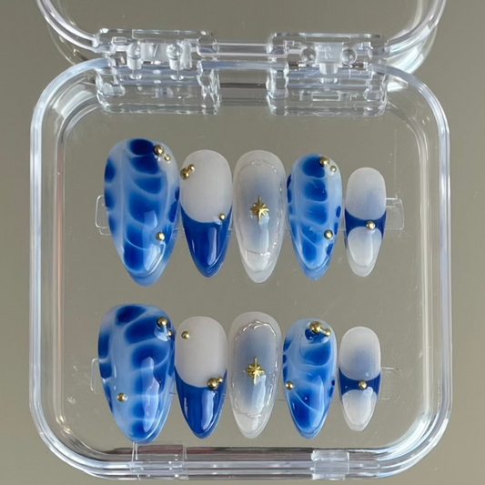 Set of dark blue and white tie dye press-on nail with gold accents in a clear case.